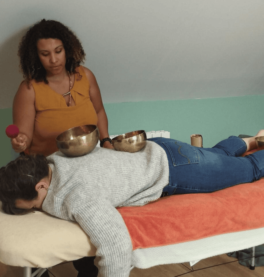 Coralie, sonothérapeute en Essonne, pratiquant un massage sonore en posant des bols tibétains sur le dos d'une cliente pour libérer les tensions énergétiques.