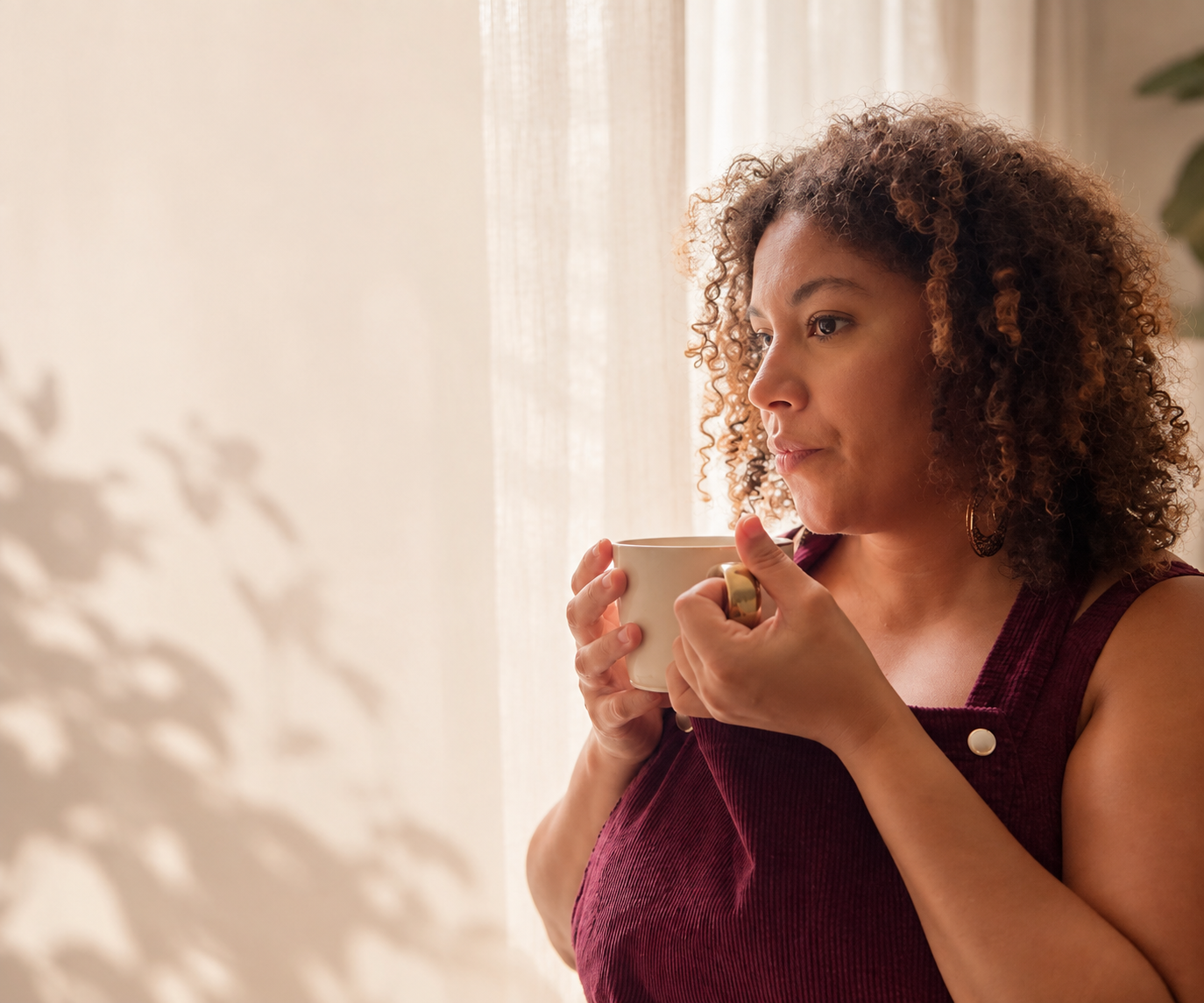 Coralie, une tasse entre les mains, près d’une fenêtre lumineuse.